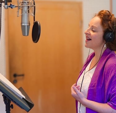 eine Frau mit violettem Schal singt im Tonstudio in ein Mikrofon