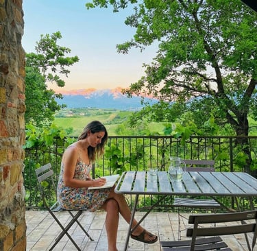 A woman journaling on a balcony with a view to Italian mountains