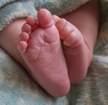 Close-up of a baby's toes peeking out from a soft blue blanket, with one foot's toes gently curled inward.