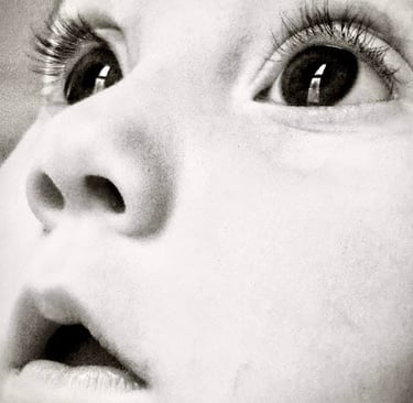 Black and white close-up of a baby girl's face, looking upward with wide eyes, capturing a sense of wonder and innocence