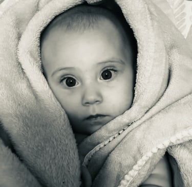 Black and white photo of a baby girl wrapped in a soft blanket, gazing at the camera with wide eyes.