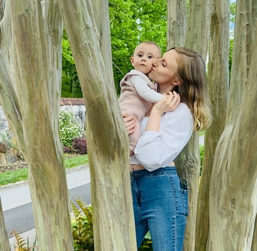 A mother holding her baby in a tree, kissing her on the cheek while the baby looks at the camera, showing loving mother-child
