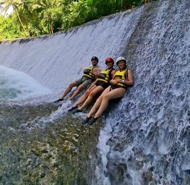 three people sitting on a waterfall in a jungle