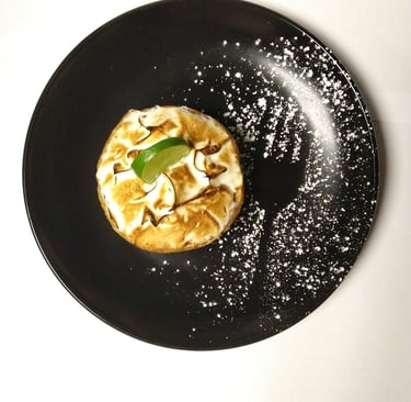 Black plate with individual dessert, containing outline of a fork and fresh lime