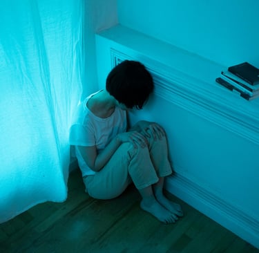 Pessoa sentada no chão da sala, demonstrando tristeza. 