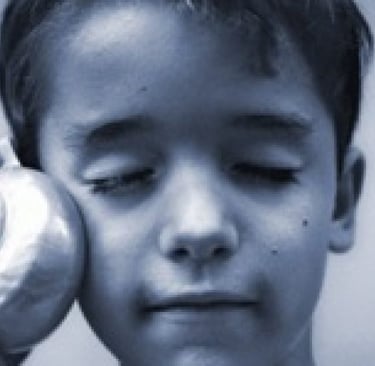 Um menino, segurando uma concha grande próxima ao ouvido, com os olhos fechados