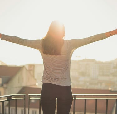 Uma mulher de pé, de braços abertos, voltada para um pôr do sol