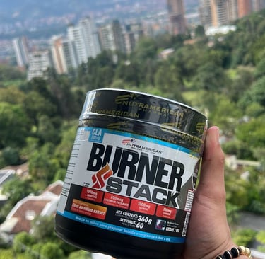 A hand holding a Nutramerican Pharma Burner Stack supplement container against a city skyline backdrop.