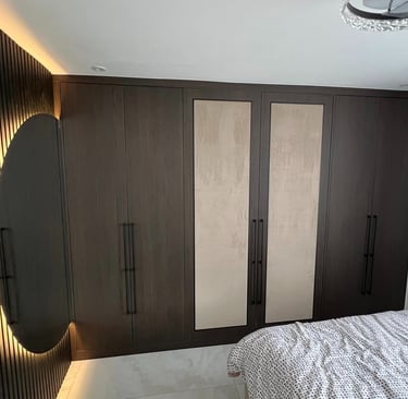 Modern dark wood fitted wardrobe with integrated lighting and a round backlit mirror in a bedroom.