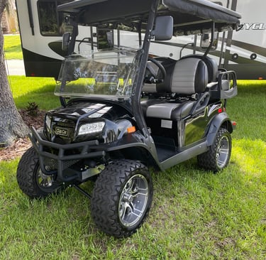 Custom black Club Car golf cart with off-road tires and lift kit parked on grass.