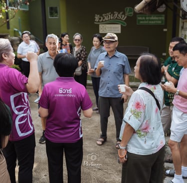 ภาพถ่ายหมู่คณะหน้าศูนย์วิสาหกิจชุมชนบ้านน้ำเกี๋ยน จังหวัดน่าน พร้อมป้ายยินดีต้อนรับและสินค้า OTOP