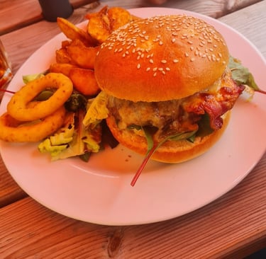 Gourmet bacon cheeseburger Black angus on a sesame seed bun served with wedges and onion rings.