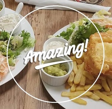 Crispy battered fish and chips served with mushy peas, tartar sauce, and side salad on a wooden table.