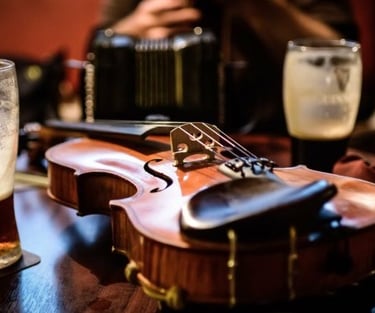 A wooden fiddle sits on a pub table alongside glasses of beer and an accordion.