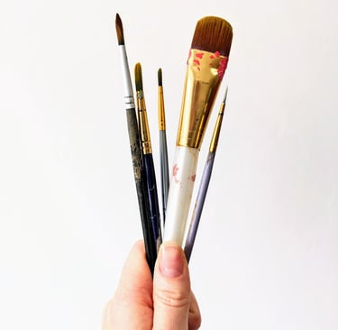 Hand holding a variety of professional artist paint brushes against a white background.