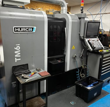 A Hurco TM6i CNC lathe machine in a precision machine shop with industrial tools and control panel.