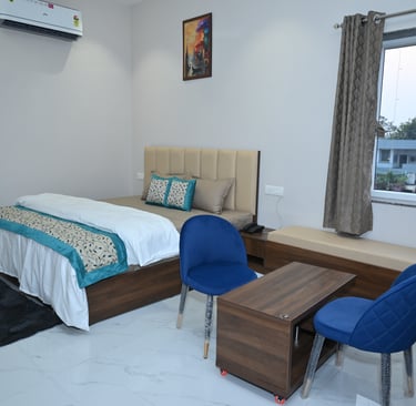 Modern hotel room with a double bed, blue chairs, wooden coffee table, and air conditioning.