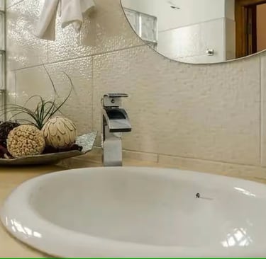 Modern bathroom vanity featuring a white drop-in sink, chrome faucet, and glass block wall.