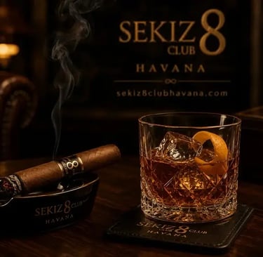 Una elegante copa de cóctel reposa sobre una mesa de madera oscura junto a un cigarro encendido.