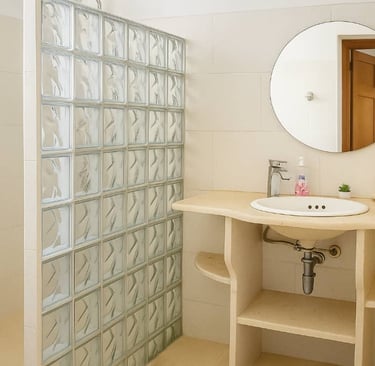 Modern bathroom featuring a glass block shower wall, round mirror, and a minimalist stone vanity.