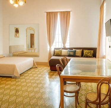 Spacious studio apartment with a bed, glass dining table, sofa, and vintage tiled flooring.