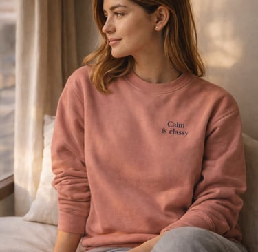 Frau sitzt am Fenster und trägt ein Dusty-Rose Sweatshirt „Calm is classy“ in ruhiger Atmosphäre.