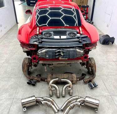 Red Porsche 911 at an auto repair shop for a high-performance exhaust system upgrade.