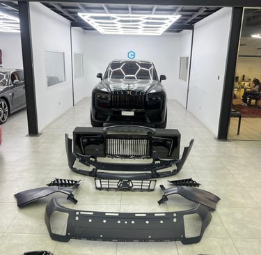 Black Rolls-Royce Cullinan in a luxury auto body shop with disassembled front bumper and grill parts.