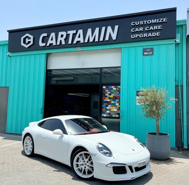 A white Porsche sports car parked outside Cartamin car care and customization shop.