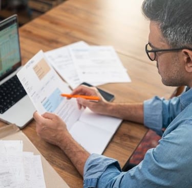 Man working diligently on paperwork, surrounded by a laptop,  and documents.