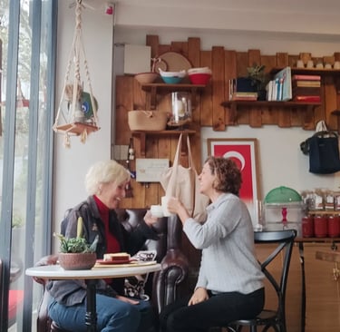 Two women emel and gülay talking and drinking coffee in a cozy rustic cafe with wooden wall decor.