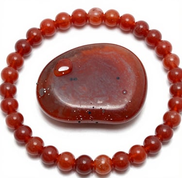 Polished red carnelian crystal worry stone surrounded by a matching beaded gemstone bracelet on a white background.