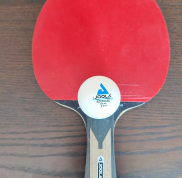 Análise de aderência e cabo ergonómico de madeira em raquete de ténis de mesa Joola com bola.