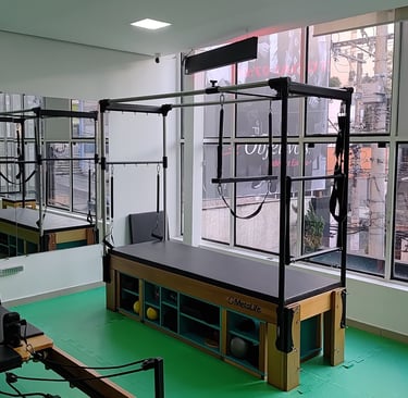 Professional Pilates Cadillac trapeze table in a bright studio with large windows and wall mirrors.