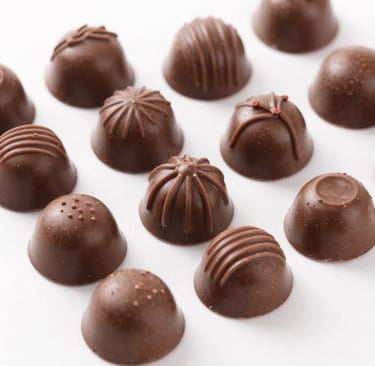 Close-up of a handcrafted dark chocolate truffle with delicate gold leaf decoration.