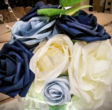 Elegant artificial flower arrangement featuring navy blue, light blue, and white roses with green leaves.