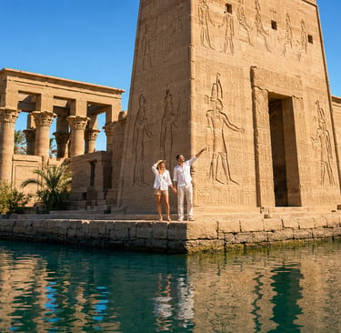 A couple tours the ancient Philae Temple in Aswan, Egypt, featuring stone hieroglyphics and pillars by the Nile River.