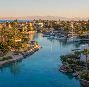 Luxury resort in El Gouna, Egypt featuring a blue lagoon, yachts in a marina, and palm trees at sunset.