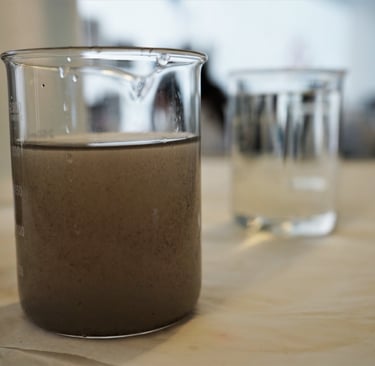 Muestra de agua turbia con sedimentos en vaso de laboratorio junto a muestra de agua filtrada clara