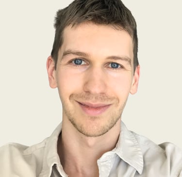 Professional headshot of a smiling young man with blue eyes and short brown hair.