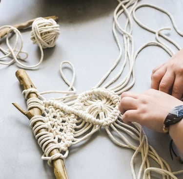 Manos creando un colgante de macramé usando cordón blanco con soporte de madera