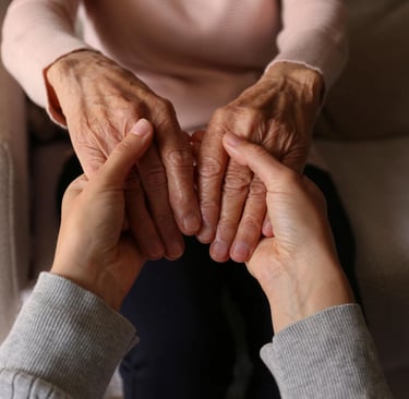 A caregiver's hands gently holding the hands of an elderly woman to show support and senior care.