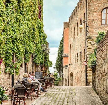 People enjoying coffee at an outdoor terrace on a charming historic street in Certaldo Alto, Tuscany