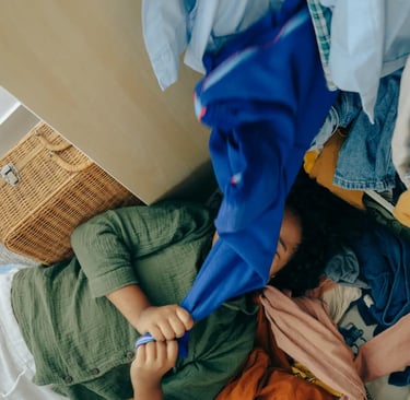 A person lying on the floor surrounded by a large pile of messy laundry and clothes.
