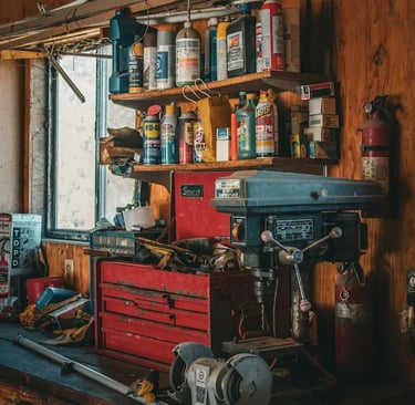 Rustic wood workshop workbench with a red metal toolbox, bench grinder, and drill press.