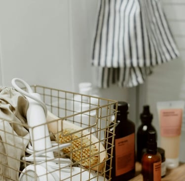 A white hair dryer and body brush in a wire storage basket on a wooden bathroom counter.