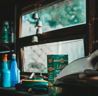 Lawn feed, weed killer, and spray bottles on a workbench in a rustic garden shed.