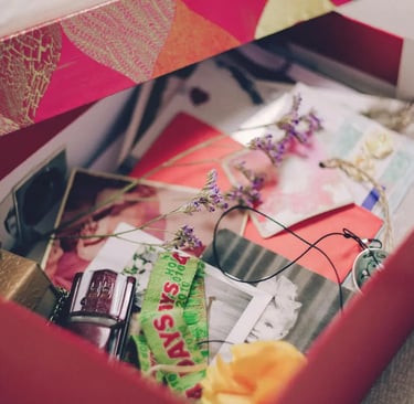 A red keepsake box filled with sentimental vintage photos, dried flowers, and small mementos.