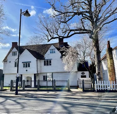 A historic white weatherboard building with gables under bare trees and a blue sky.