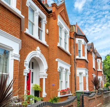Rows of Victorian red brick terraced houses on a suburban London street under a blue sky.